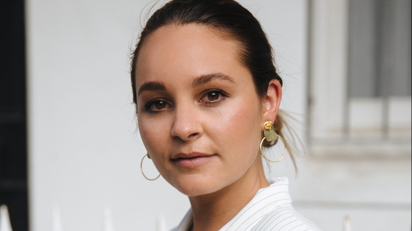 Beck Wadworth, founder of An Organised Life, is pictured wearing a white blazer with black pinstripes. She wears gold earrings and a gold necklace, and is looking at the camera smiling. Her hair is in a bun.