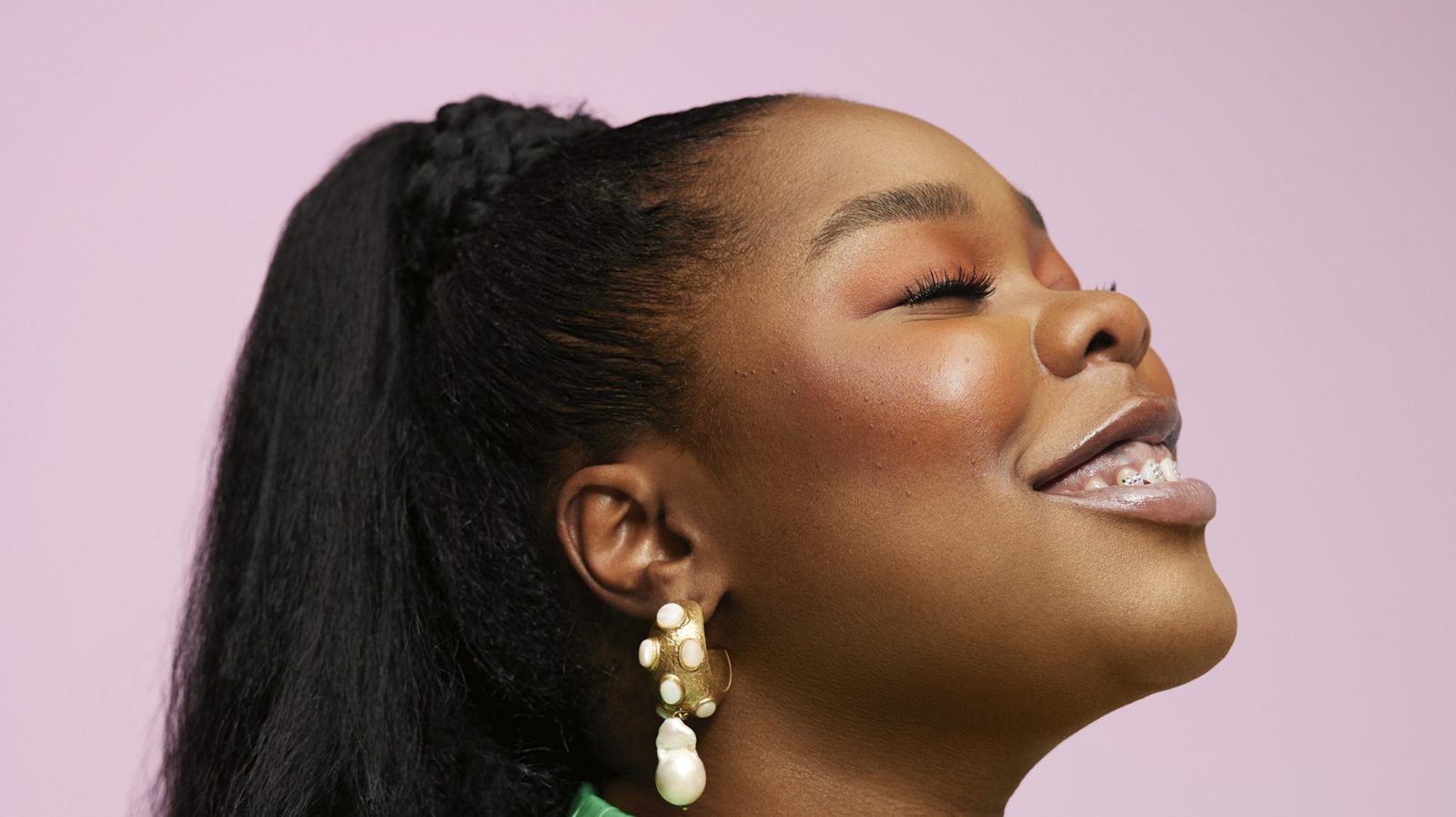 Lillian Ahenkan is pictured wearing a light green plisse top. Her hair is in a ponytail and she is wear gold earrings. She is pictured on her side, and she is smiling up at the sky.