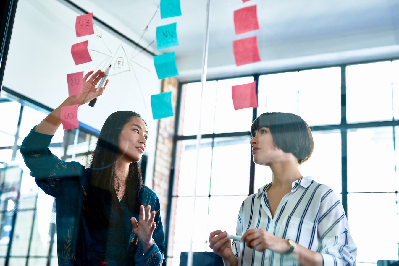 Two women discuss goal setting using sticky notes on a glass wall