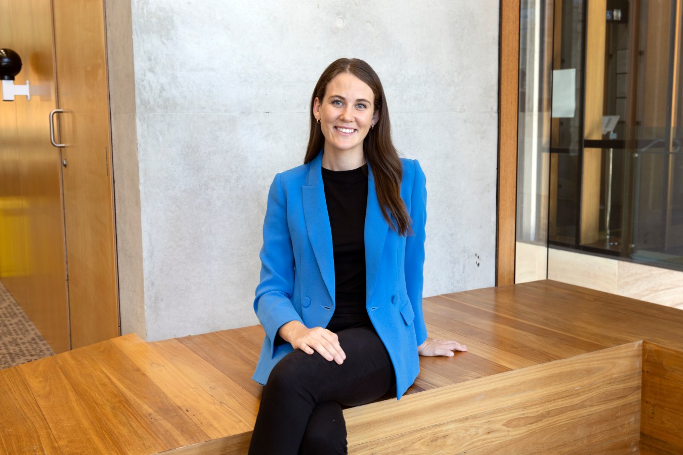 Hailey Brown is the CEO and founder of Vacayit. She is pictured wearing a black top, black pants and a cobalt blue blazer. Her hair is brown and she wears it down.