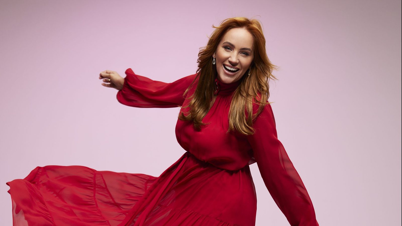 Jules Robinson is wearing a long, red dress. She is dancing, and has her arms out to the side.