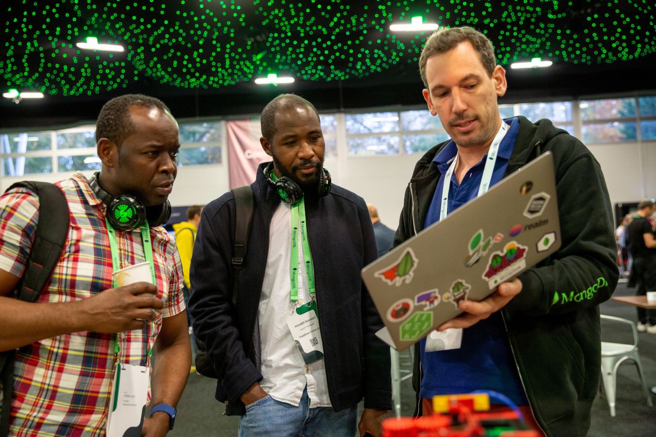 Two men watch a demonstration by another man holding a laptop computer.