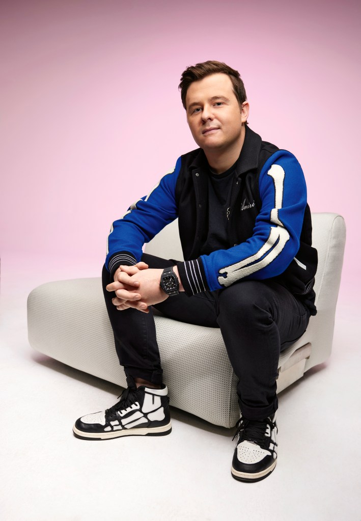 Elliot Watkins is sitting down on a white boucle chair.