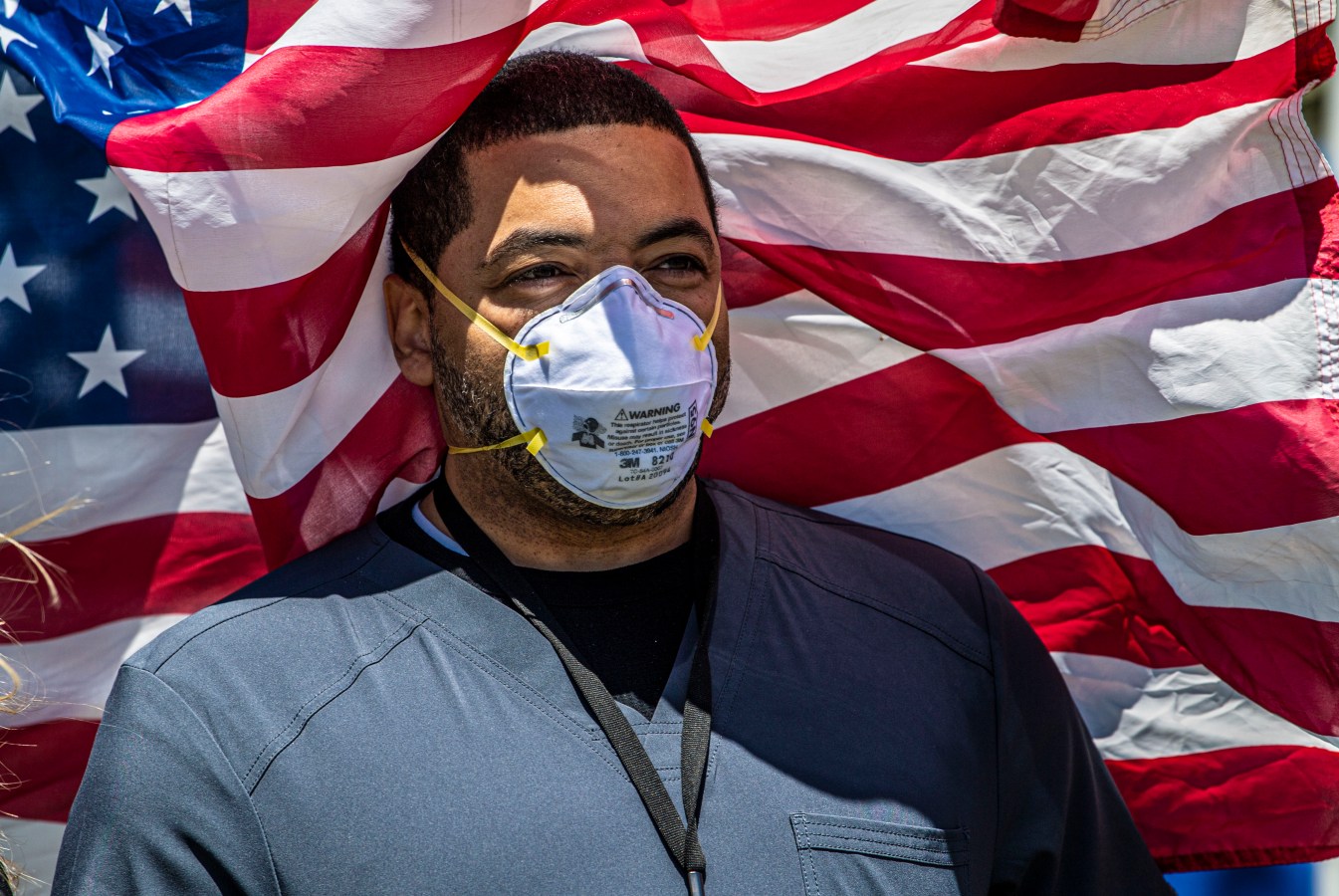 Nurse poses in front of American flag during salute to healthcare workers on Long Island