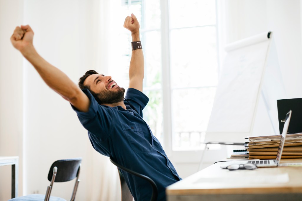 Man sitting at desk with laptop computer and stretching arms above his head