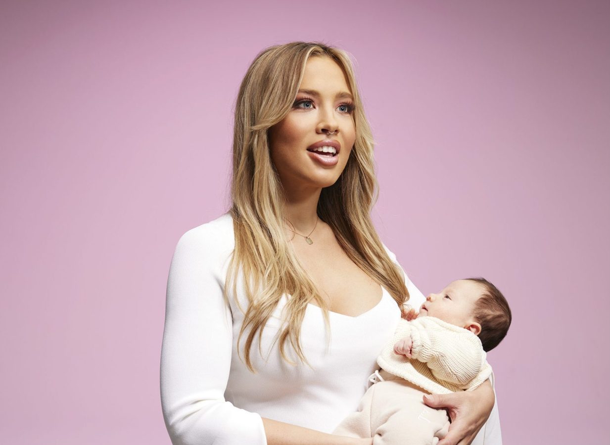 Tammy Hembrow is wearing a white dress. She is holder her daughter, Posie.