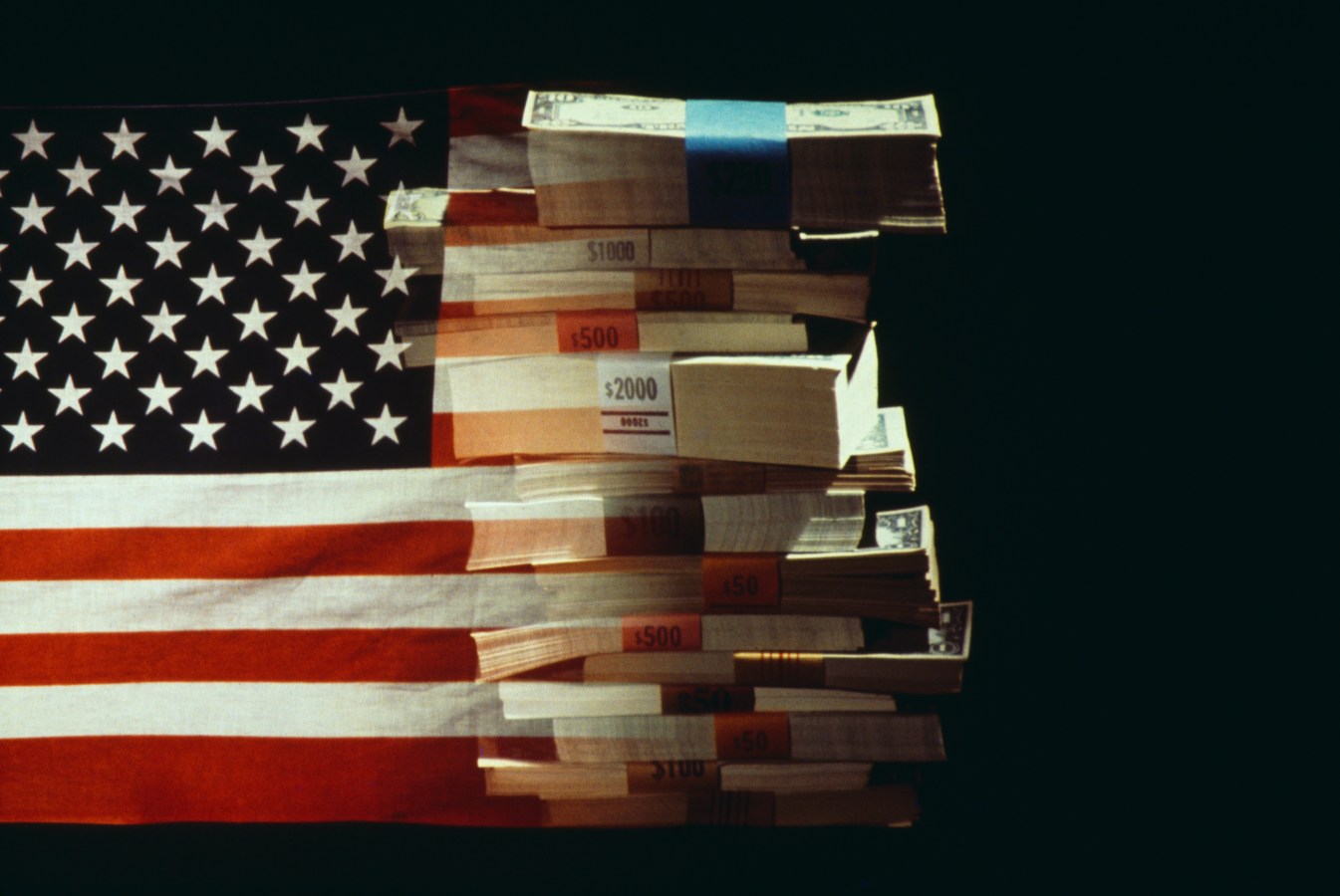 The American flag superimposed over a pile of American dollars banknotes