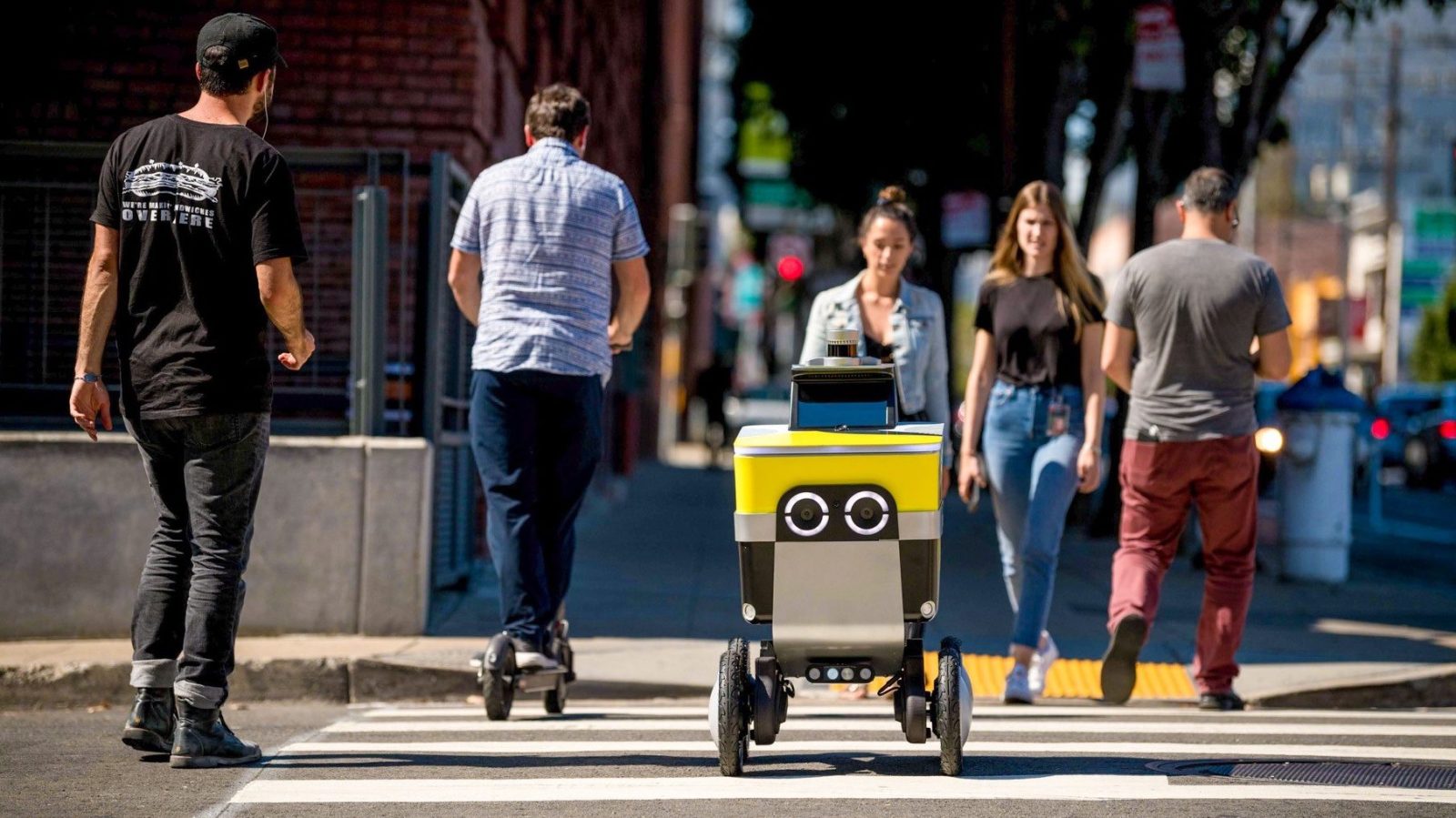 Uber Eats delivery robot crossing at a pedestrian crossing with people around