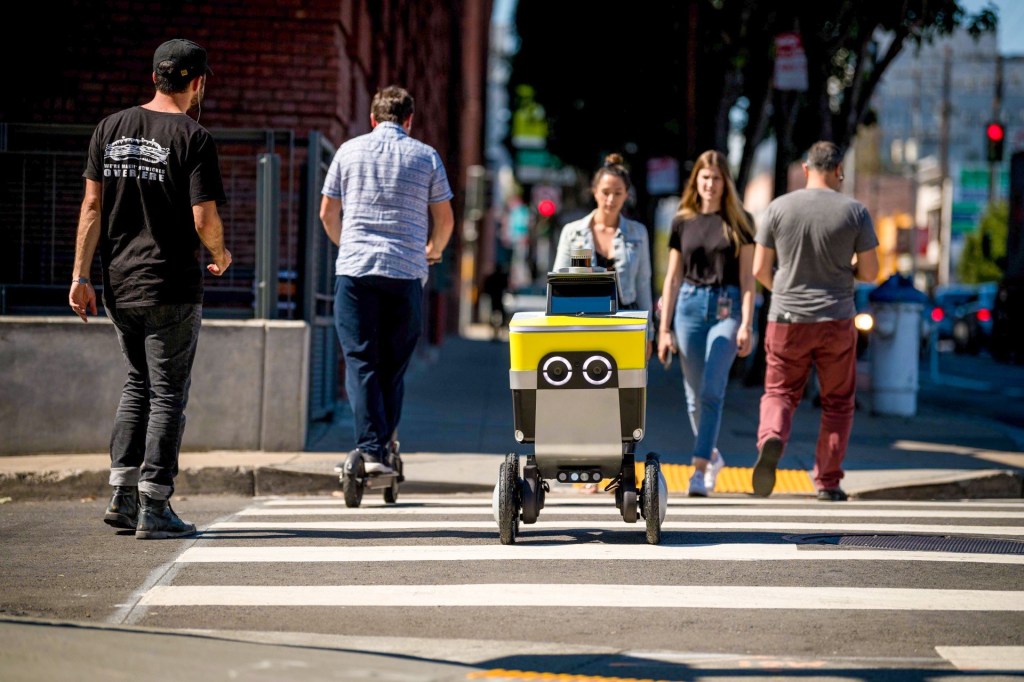 Uber Eats delivery robot crossing at a pedestrian crossing with people around