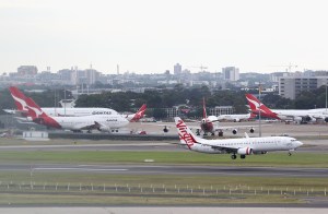 Virgin Australia plane taking off at airport with Qantas aircraft parked behind