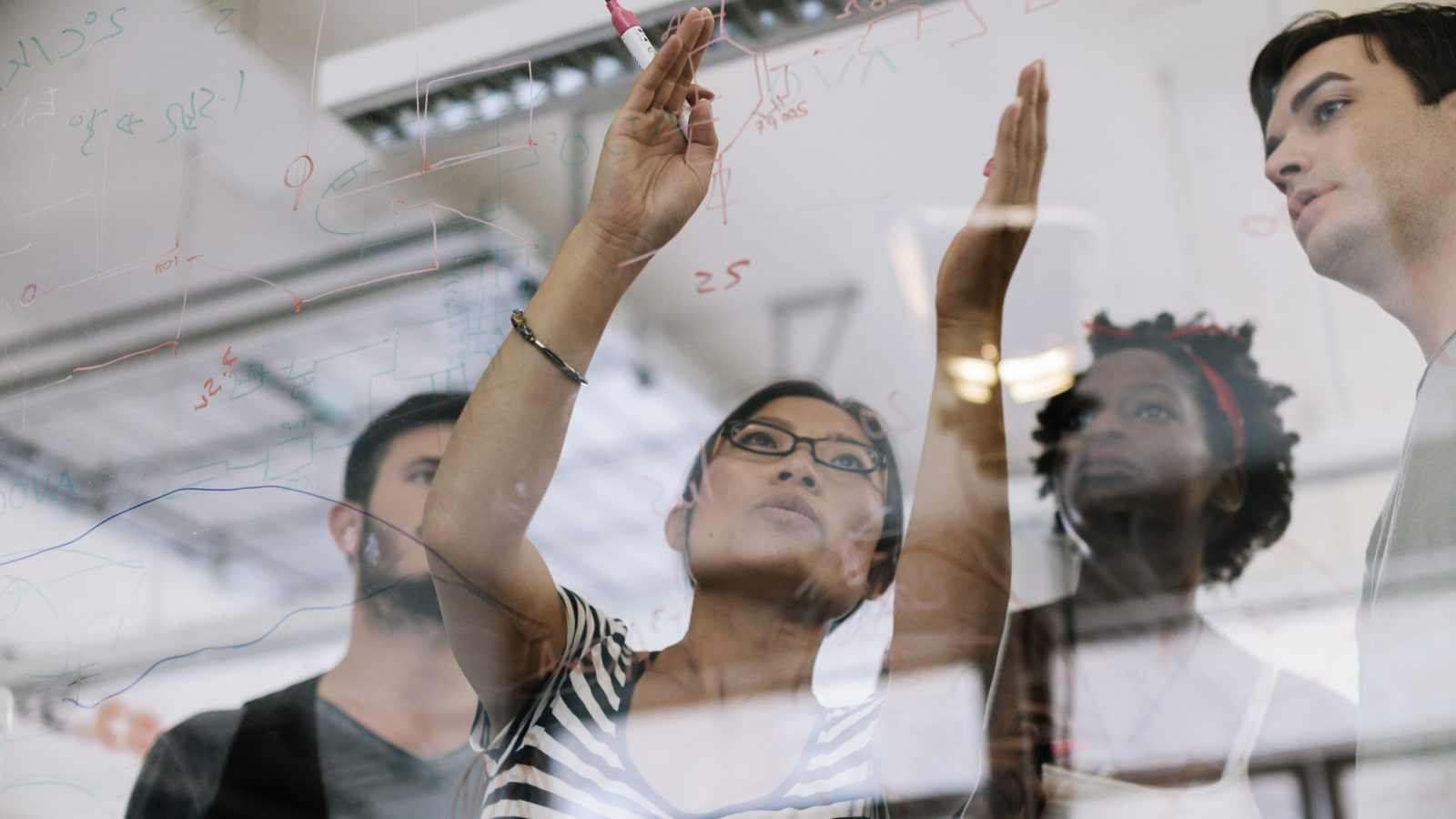 Asian woman leading the discussing of an electronic project. she pointing to electronic schematic on a glass wall