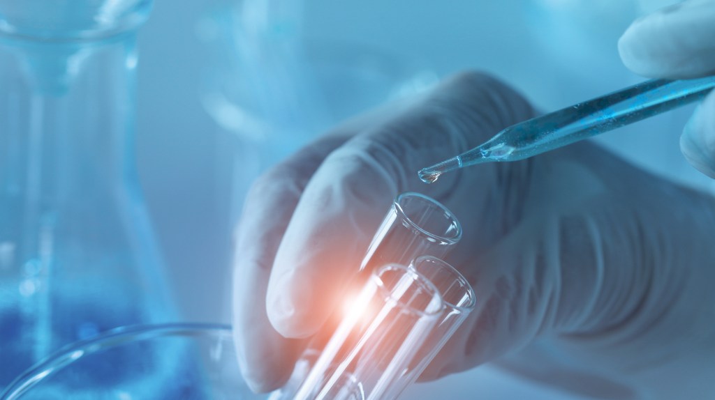 dropper adding liquid to a test tube held in gloved hand