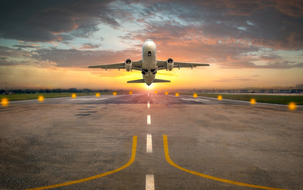 Airplane taking off from an airport runway in sunset light | Image source: Getty Images