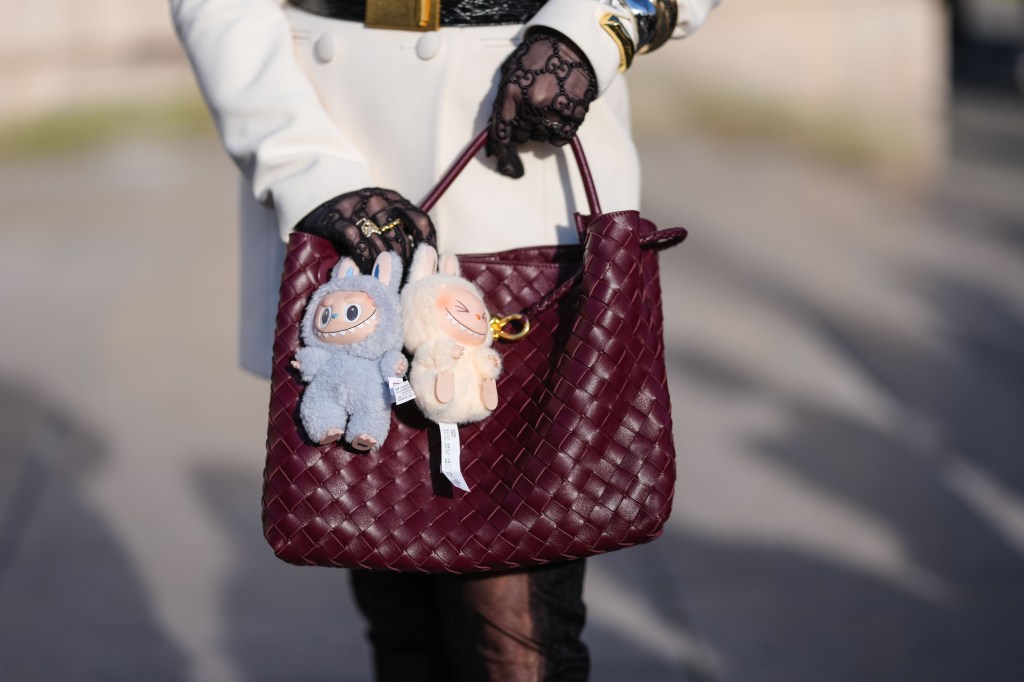 A guest wears a burgundy bordeaux woven Bottega Veneta Andiamo leather bag, light blue Labubu bag charm, cream Labubu bag charm, outside Elie Saab, during the Paris Fashion week Women's Fall/Winter 2025-2026 on March 8, 2025 in Paris, France. (Photo by Edward Berthelot/Getty Images)