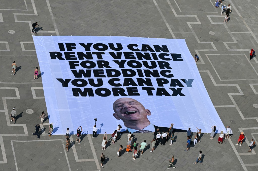 Activists of international environmental group Greenpeace deploy a giant banner displaying a picture of Jeff Bezos and reading "If you can rent Venice for your wedding you can pay more tax" at St Mark square  in Venice on June 23, 2025. 