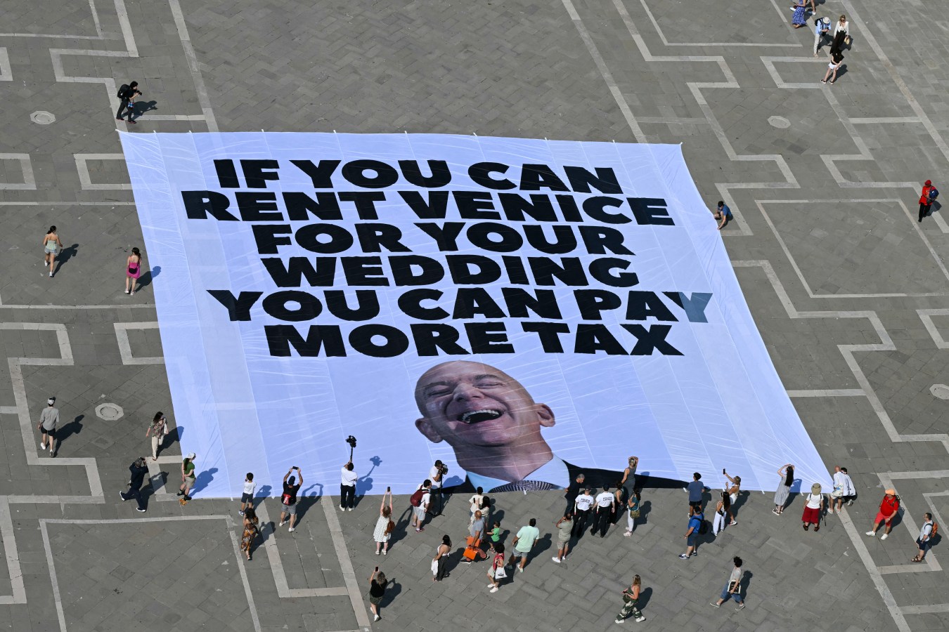 Activists of international environmental group Greenpeace deploy a giant banner displaying a picture of Jeff Bezos and reading "If you can rent Venice for your wedding you can pay more tax" at St Mark square in Venice on June 23, 2025.